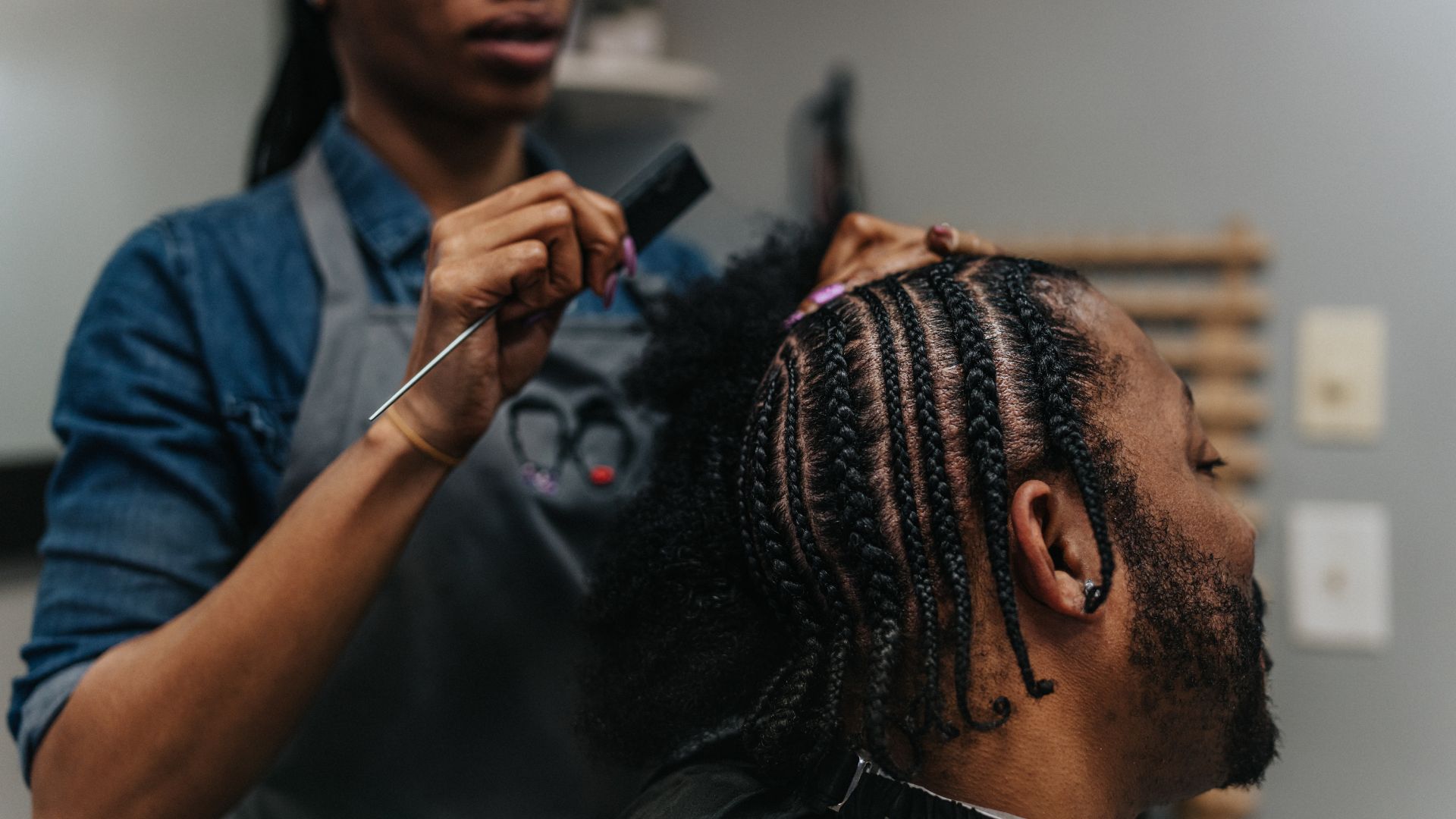 Hairstylist braiding cornrows for client in professional salon setting