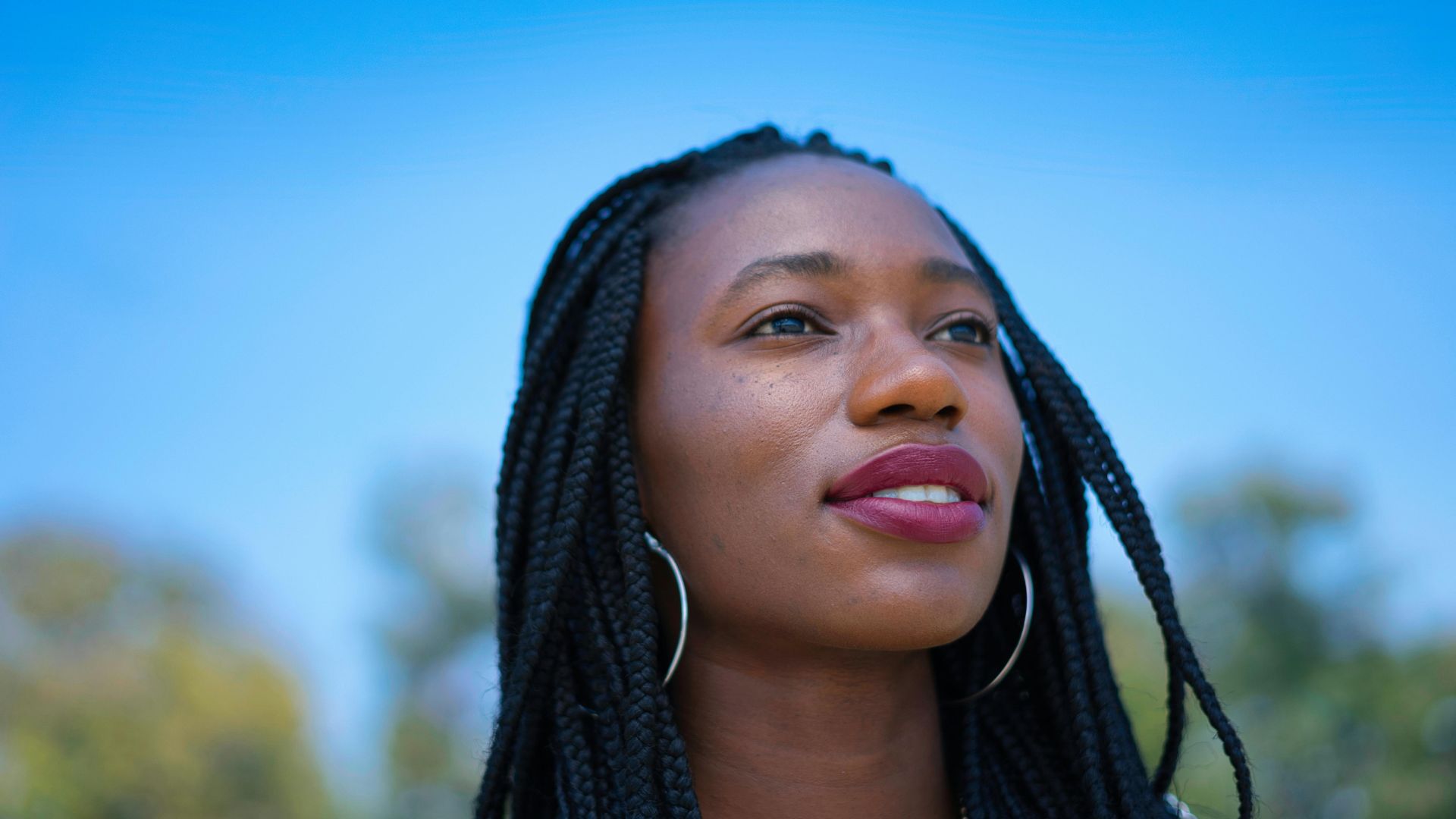 Woman with braids looking upward against blue sky and blurred background